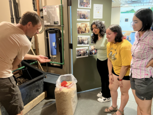 One contractor showing three students some of the finer points of the composting toilet bin in the basement.